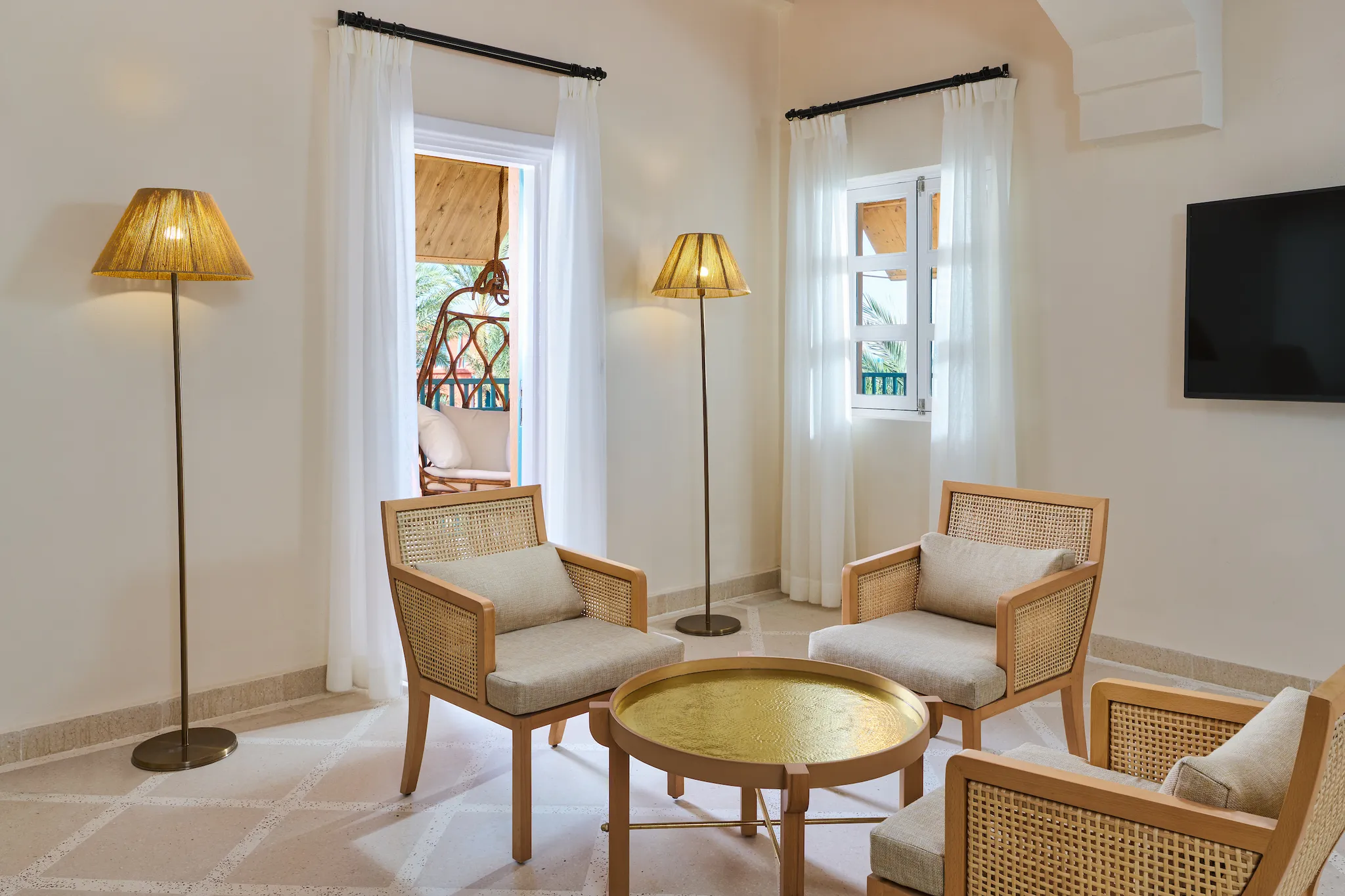 Superior Suite living area with rattan armchairs, brass coffee table, floor lamps, and doorway leading to the balcony at Sheraton Miramar Resort El Gouna