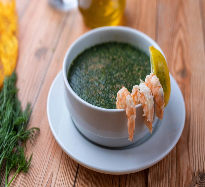 A bowl of Molokhia with shrimps, featuring a rich and flavorful green soup made from finely chopped jute leaves, garnished with succulent, perfectly cooked shrimp, served hot and accompanied by a side of steamed rice or bread.