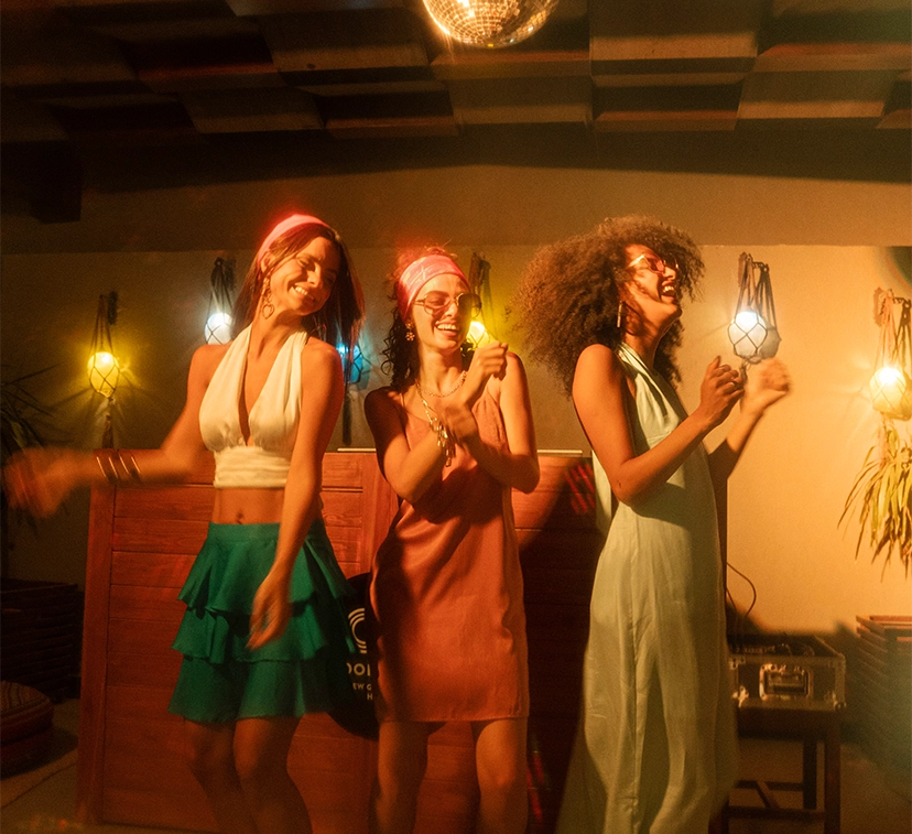 Three women dancing energetically at a vibrant Gouna venue, surrounded by colorful lighting and a lively atmosphere, showcasing joy and cultural celebration.