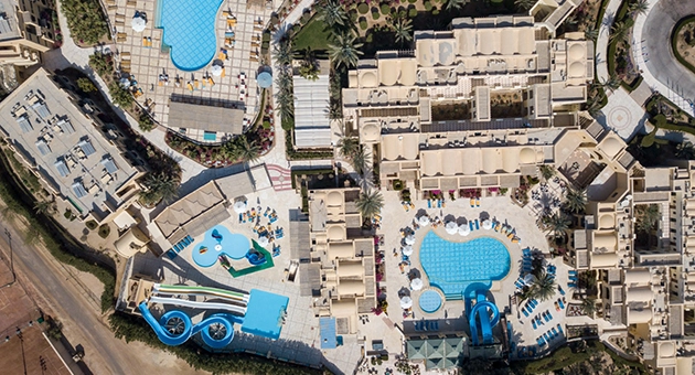 Aerial view of the hotel with multiple swimming pools visible, surrounded by lush greenery and well-designed outdoor spaces.