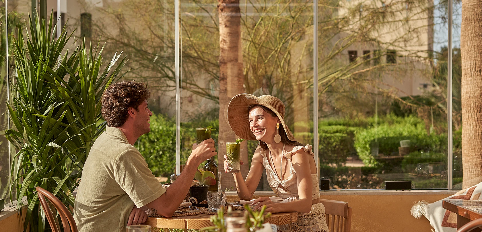 A couple enjoying the dining experience at The Three Corners Rihana Resort. They are seated at an elegantly set table with drinks. The stylish and inviting ambiance enhances their dining experience.