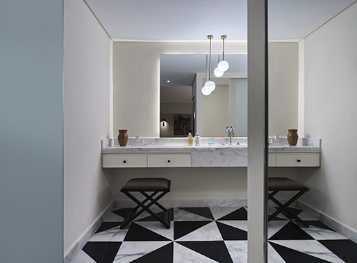Bathroom of the Garden Suite at Chedi El Gouna Red Sea, showing a modern design with a mirror above a sleek vanity, a contemporary cabinet for storage, and a comfortable chair. The space is well-lit and designed for functionality, featuring clean lines and elegant finishes.