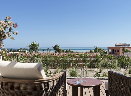 Seaside sitting area on the beach with comfortable chairs and tables, overlooking the ocean and clear blue sky.