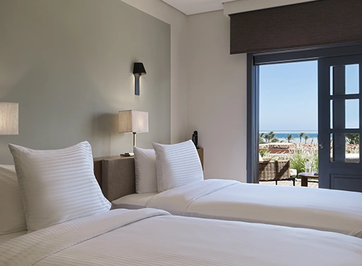 Superior Sea View Twin Room at El Gouna Red Sea, featuring two twin beds with white linens, a private balcony offering panoramic views of the Red Sea, and modern, stylish furnishings. The room is bright and airy, designed for comfort and relaxation, with large windows allowing natural light to fill the space.