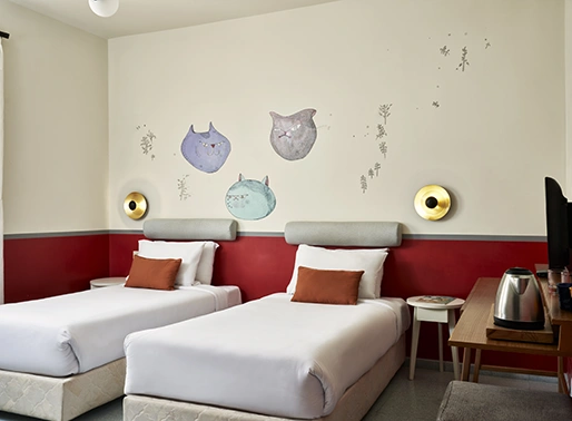 Two twin beds with vibrant red headboards in the Fire Room at Turtles Inn, El Gouna, Red Sea, Egypt. The room features warm, earthy tones, a natural light, and minimalist style, creating a cozy and inviting atmosphere.